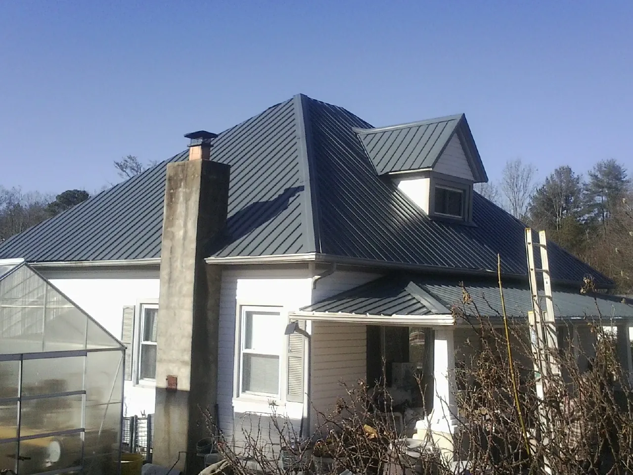 Dark blue standing seam metal roof on a white farmhouse with dormer — Slate & Tile Roof Repair by Roofing Brothers in Highmore