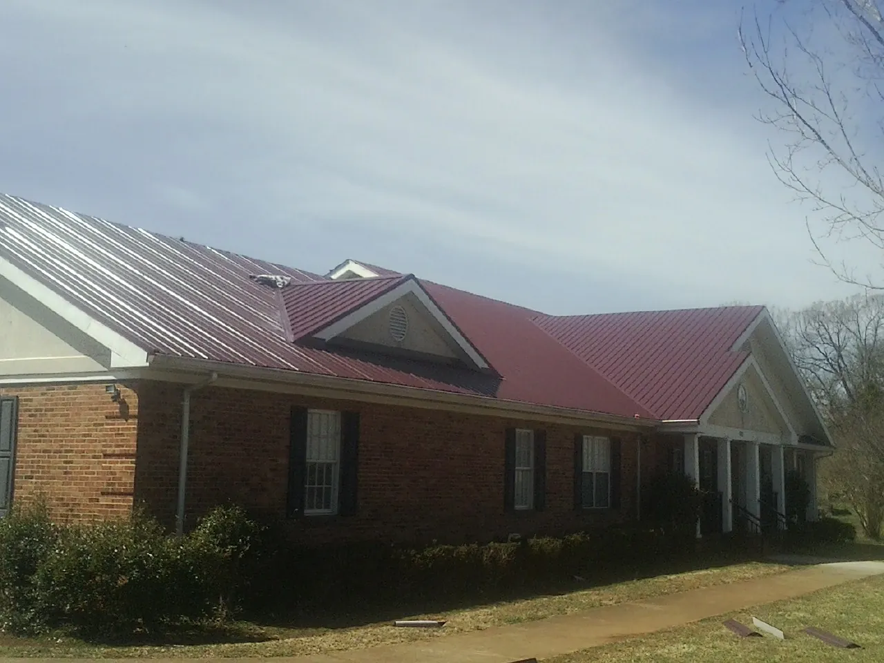 Red metal roof with gabled entries on a long brick building, from a Hail Damage Roof Repair job in Highmore