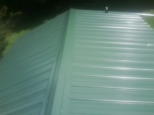 New green metal panels meeting at the ridge of a roof — Flat Roof Repair work by our crew in Highmore