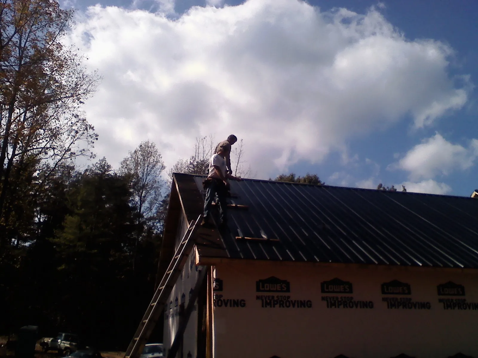 Roofer fastening dark metal panels high against a cloudy sky, from a Roof Inspection job in Highmore